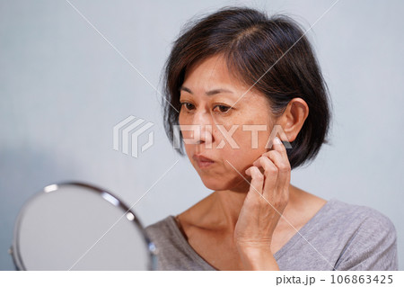 頬に手をやるシミ、シワのある老け顔の中年女性 106863425