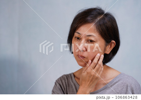 頬に手をやるシミ、シワのある老け顔の中年女性 106863428