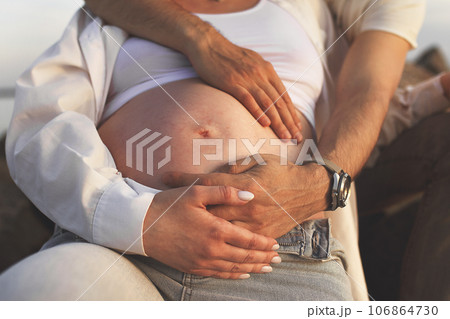 unrecognizable body of pregnant woman in casual and hands of parents intertwined on stomach unrecognizable body of pregnant woman in casual and hands of parents intertwined on stomach 106864730