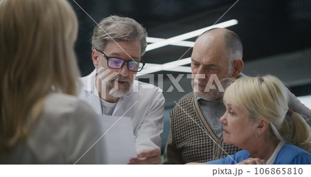 Mature doctor talks to elderly couple at reception Mature doctor talks to elderly couple at reception 106865810