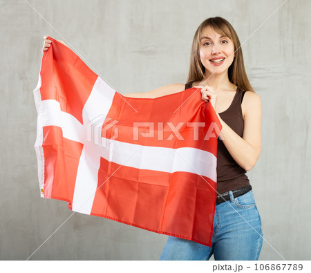 Happy young woman holding flag of Denmark against unicoloured background 106867789