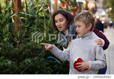 Mother and preteen son choosing New Year fir tree on outdoor fair Mother and preteen son choosing New Year fir tree on outdoor fair 106868082