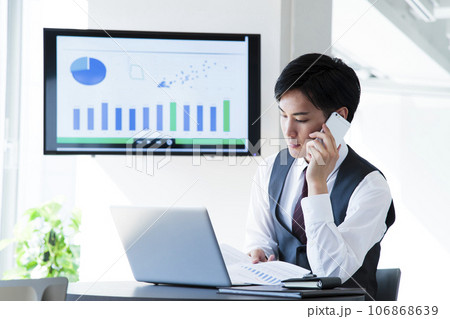 オフィスでスマホとパソコンを操作して仕事をする若いビジネスマン 106868639