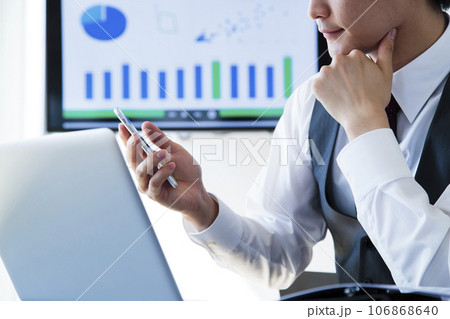 オフィスでスマホとパソコンを操作して仕事をする若いビジネスマン 106868640