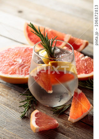 Gin tonic with ice, rosemary, and grapefruit slices on an old wooden table. 106872813