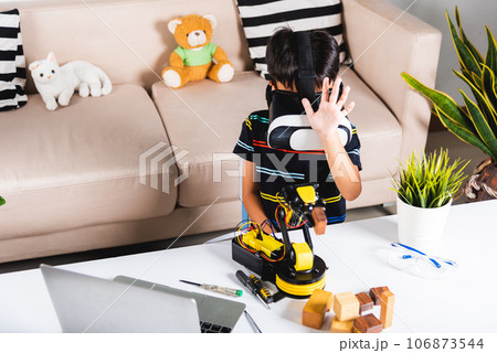 Asian kid boy using VR glasses on robotic arm in workshop, Child learning programer control robot arm with sensors to pick up wood block, Technology education, Virtual Reality Simulator, industry 4.0 106873544