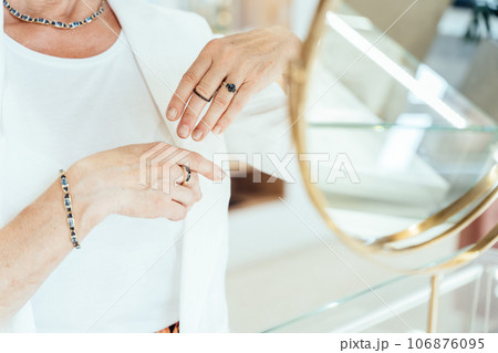 Unrecognizable mature old woman pensioner admiring his reflection in the mirror in jewelry store. Unrecognizable mature old woman pensioner admiring his reflection in the mirror in jewelry store. 106876095