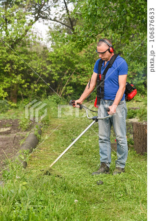 Man mowing tall grass. Process of lawn trimming with hand mower. 106876633
