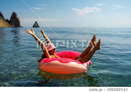 Summer vacation woman in hat floats on an inflatable donut mattress. Happy woman relaxing and enjoying family summer travel holidays travel on the sea. Summer vacation woman in hat floats on an inflatable donut mattress. Happy woman relaxing and enjoying family summer travel holidays travel on the sea. 106880542