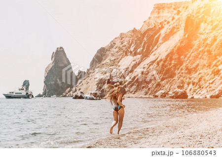 Woman travel summer sea. A happy tourist in a blue bikini enjoying the scenic view of the sea and volcanic mountains while taking pictures to capture the memories of her travel adventure. 106880543