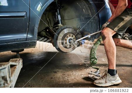 Close up of strong, hardworking worker changing car wheel, holding equipment. Worker, mechanic, repairman repairing, fixing car, working in auto center. Concept of car repairing. Close up of strong, hardworking worker changing car wheel, holding equipment. Worker, mechanic, repairman repairing, fixing car, working in auto center. Concept of car repairing. 106881922