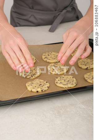 teenager boy's hands put raw american chocolate chip cookies on baking sheet. vertical shot of young chef hands making cookies 106883467