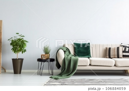 Beige sofa with green blanket and cushions standing against white, empty wall in minimalistic living room 106884059
