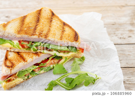 Panini sandwich with ham, cheese, tomato and arugula on wooden table 106885960
