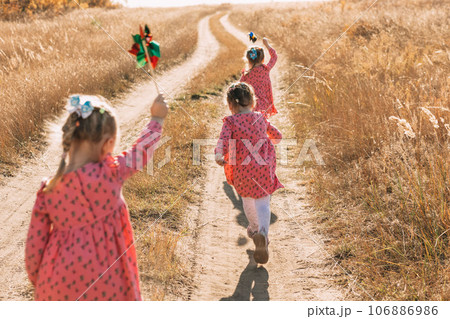 Playing in the wind: triplet girls run towards adventures with windmills on a warm autumn day, using wind energy 106886986