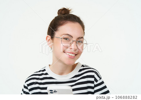 Image of young woman in glasses, using her mobile phone, standing with smartphone and smiling, standing over white background Image of young woman in glasses, using her mobile phone, standing with smartphone and smiling, standing over white background 106888282