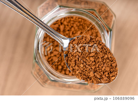 Top view on spoon with instant granulated coffee over a jar on a wooden background. 106889096