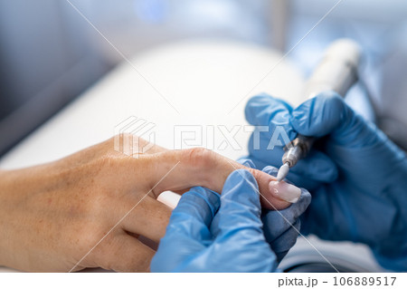 Nail care procedure in a beauty salon. Female hands and tools for manicure, process of performing manicure in beauty salon. Concept spa body care. Gloved hands of a skilled manicurist cutting cuticles Nail care procedure in a beauty salon. Female hands and tools for manicure, process of performing manicure in beauty salon. Concept spa body care. Gloved hands of a skilled manicurist cutting cuticles 106889517