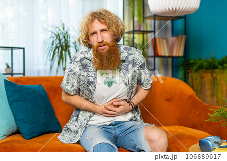 Redhead man sits on sofa feeling sudden strong abdominal stomach ache, gastritis problem, diarrhea Redhead man sits on sofa feeling sudden strong abdominal stomach ache, gastritis problem, diarrhea 106889617