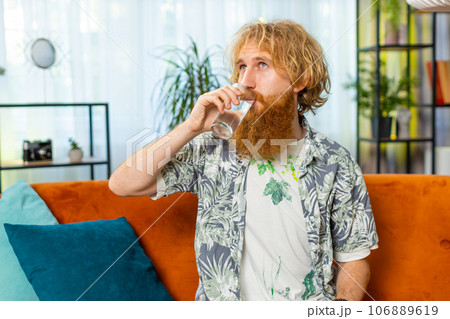 Thirsty Caucasian man sits at home holding glass of natural aqua make sips drinking filtered water 106889619