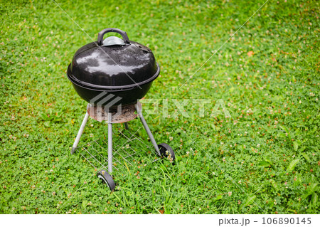 Black grill in the backyard rain green field. Preparing for barbeque party. Black grill in the backyard rain green field. Preparing for barbeque party. 106890145