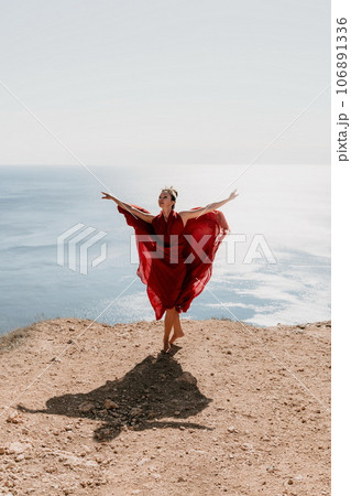 Woman in red dress on sea. Side view a Young beautiful sensual woman in a red long dress posing on a rock high above the sea on sunset. Girl on the nature on blue sky background. Fashion photo. Woman in red dress on sea. Side view a Young beautiful sensual woman in a red long dress posing on a rock high above the sea on sunset. Girl on the nature on blue sky background. Fashion photo. 106891336