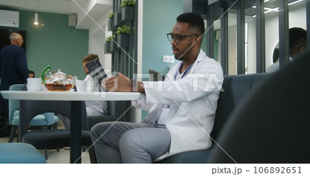 African American doctor sits in clinic cafe, consults patient via video call 106892651