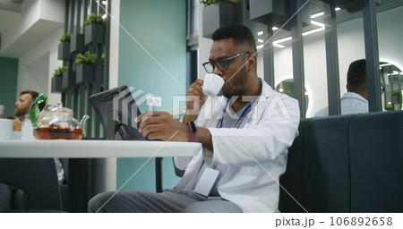 Doctor drinks tea, watches medical tests results on tablet in clinic cafe Doctor drinks tea, watches medical tests results on tablet in clinic cafe 106892658