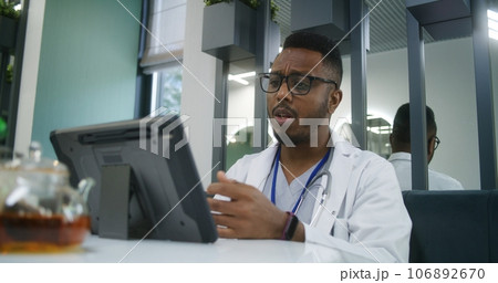 Doctor sits in hospital cafeteria, has online appointment on digital tablet Doctor sits in hospital cafeteria, has online appointment on digital tablet 106892670