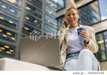 Focused woman manager talking with client and work on laptop on modern office building background 106893306