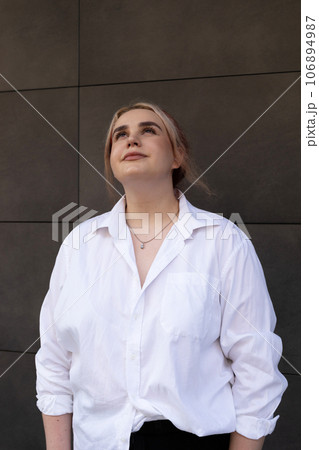 Real Young Beautiful 20s Woman, Student Looks Up. Stylish Carefree Pretty Girl Stands Outdoor, Modern Wall Of Building On Background. Generation G. Female Wears Casual Clothing. Vertical Plane. Real Young Beautiful 20s Woman, Student Looks Up. Stylish Carefree Pretty Girl Stands Outdoor, Modern Wall Of Building On Background. Generation G. Female Wears Casual Clothing. Vertical Plane. 106894987