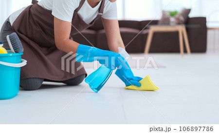 Maid wearing gloves and using cleaner spray and microfiber cloth to wipe a dust on the floor Maid wearing gloves and using cleaner spray and microfiber cloth to wipe a dust on the floor 106897786