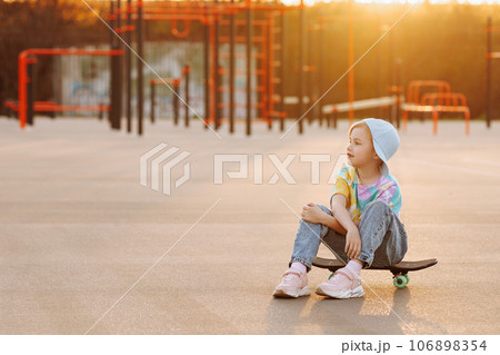 A child or girl skater sits on a skateboard. A child or girl skater sits on a skateboard. 106898354