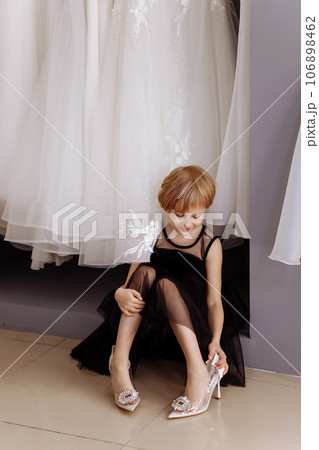 Little girl in a black evening dress in a clothing boutique Little girl in a black evening dress in a clothing boutique 106898462