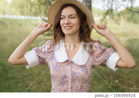 A young beautiful woman in a dress and holding a hat with her hands and reading a book in nature. Romantic and vintage photo of a beautiful girl. Reading and relaxation 106898928