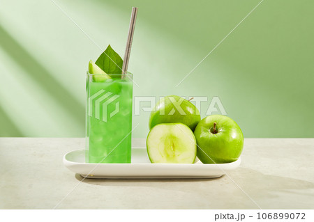 Delicious green apple juice filled in a glass. Fresh green apples displayed next to it on white dish. Green Apple (Malus domestica) contains a lot of fiber and minerals 106899072