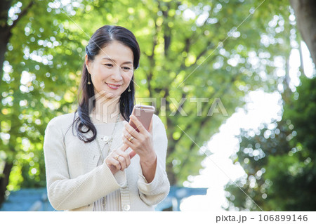 スマホを見ながら公園を散歩するミドルの女性 106899146