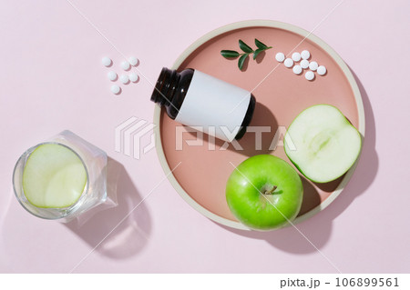 On a pink ceramic dishes, unlabeled bottle with green apples decorated. Concept for advertising product extracted from green apple, rich in vitamins, fiber and minerals On a pink ceramic dishes, unlabeled bottle with green apples decorated. Concept for advertising product extracted from green apple, rich in vitamins, fiber and minerals 106899561