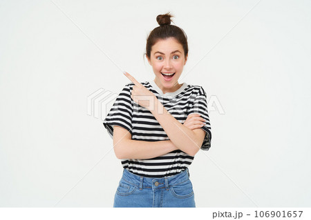 Image of excited young woman, smiling, showing amazing price discounts, pointing left, demonstrating something awesome, standing over white background 106901657