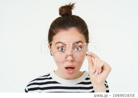 Image of woman in glasses, looks surprised, takes off eyewear, looks amazed, says wow, impressed by something, stands over white background 106901658
