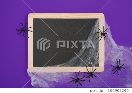 Blank black chalkboard with white cobwebs and black spiders on a purple background. A place for your text. 106902240