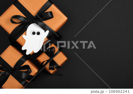 Orange gift boxes with black ribbons and a decorative ghost on a black background, Halloween presents Orange gift boxes with black ribbons and a decorative ghost on a black background, Halloween presents 106902241