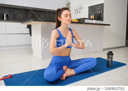 Sport and recreation. Close up portrait of beautiful girl does yoga at home, clasps her hands and meditates, sits on rubber mat in kitchen, makes asana, relaxing 106902781