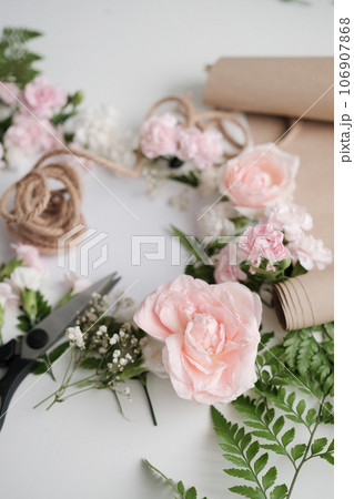 Fresh blossoming flowers and scissors on florist workspace, preparation for decorating a bouquet of flowers for the holiday Fresh blossoming flowers and scissors on florist workspace, preparation for decorating a bouquet of flowers for the holiday 106907868