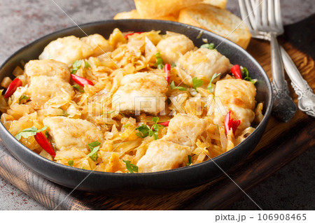Delicious spicy stewed white cabbage with sea fish fillet, onion and chili pepper close-up in a plate on the table. horizontal 106908465