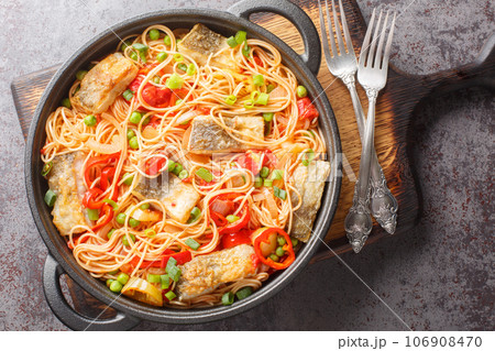 Delicious spaghetti with white fish fillet, pepper, onion, green peas and tomato sauce close-up in a frying pan. Horizontal top view 106908470