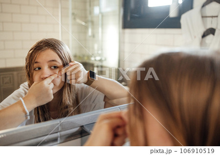 Cute teenage girl squeezes out a pimple on her cheek in the bathroom. 106910519