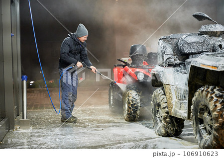Full length of man cleaning quad bike with high pressure water sprayer at self-service car washing station 106910623
