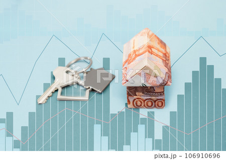 Close up of paper origami house made of Russian rubles. Light blue background with charts. The concept of mortgages and purchase of housing 106910696