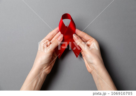 Woman's hands hold a red ribbon, a symbol of the fight against AIDS. Gray background. Copy space. Flat lay. The concept of world AIDS day 106910705